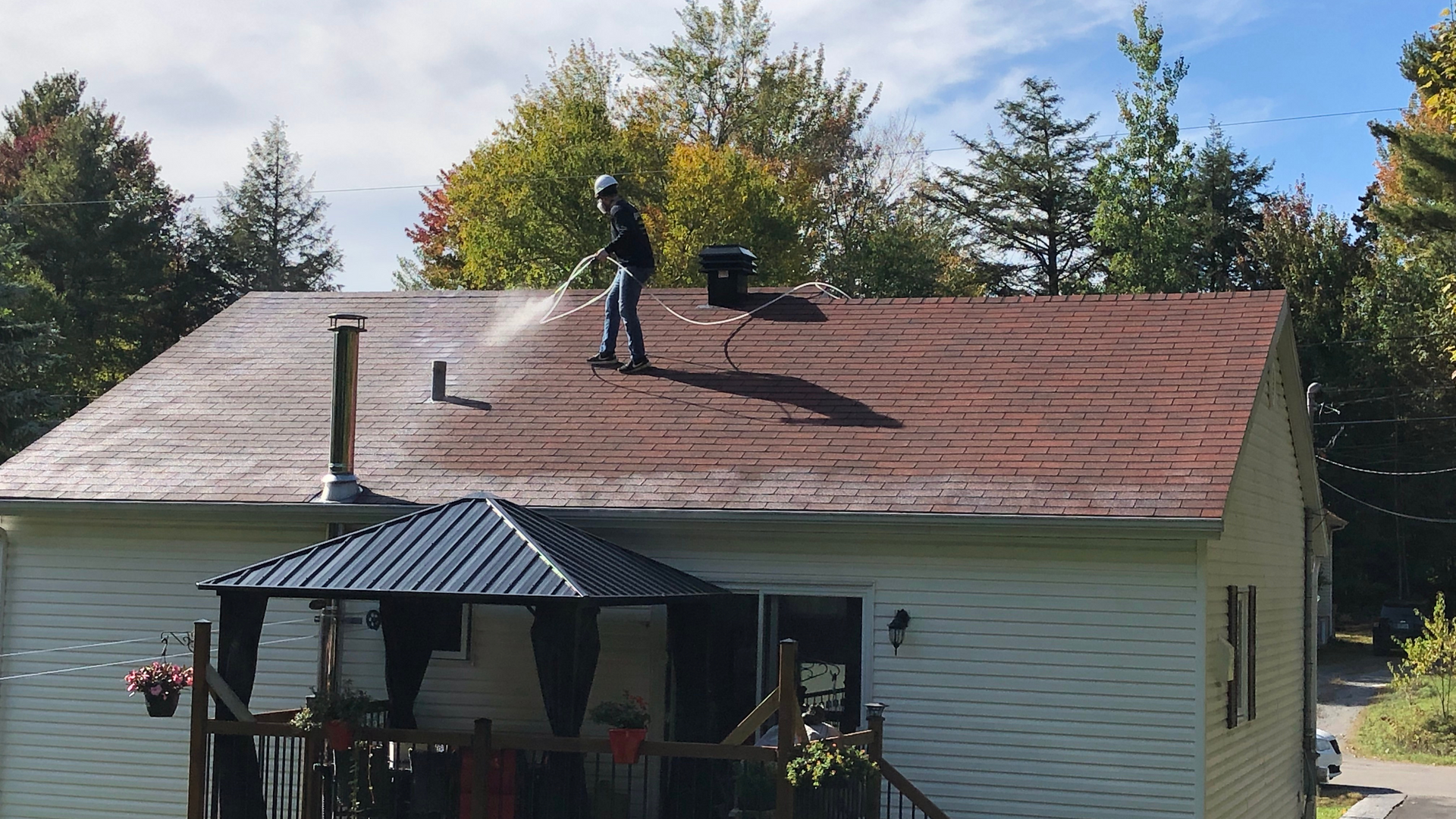 A man is cleaning the roof of a house with a pressure washer.