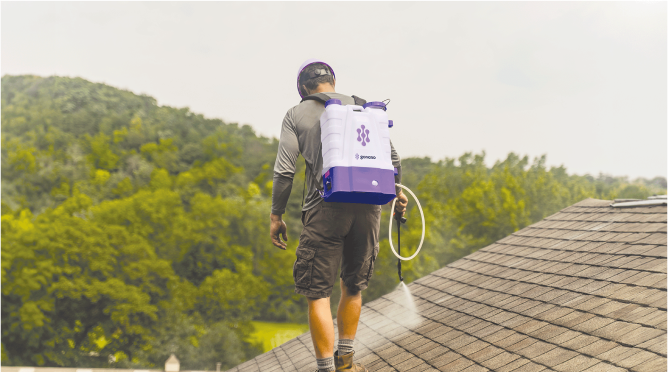 A man is spraying a roof with a backpack.
