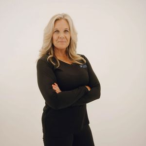 Woman with blonde hair wearing black scrubs, arms crossed.
