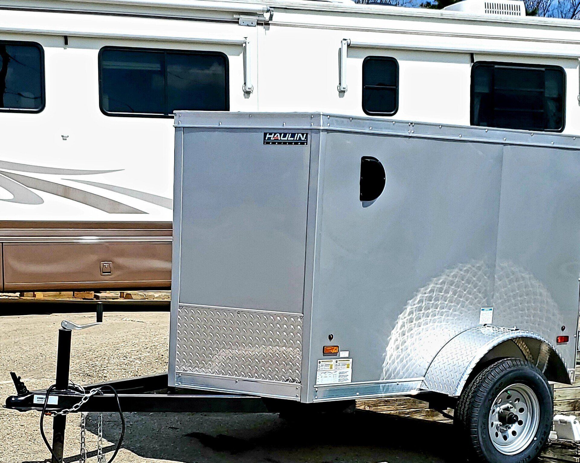 A silver trailer is parked in front of a white rv