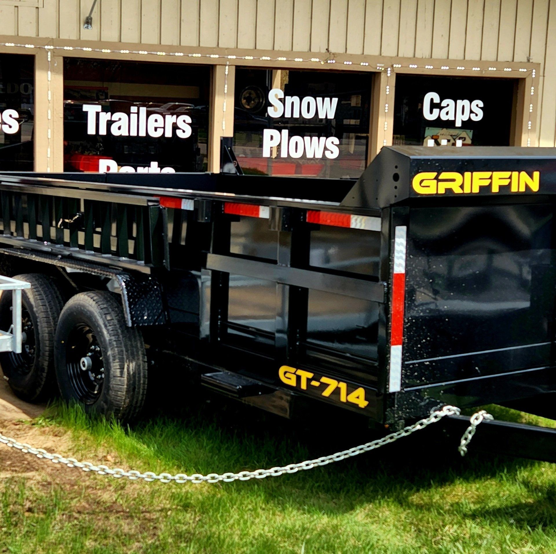 A griffin trailer is parked in front of a store that sells trailers and snow plows