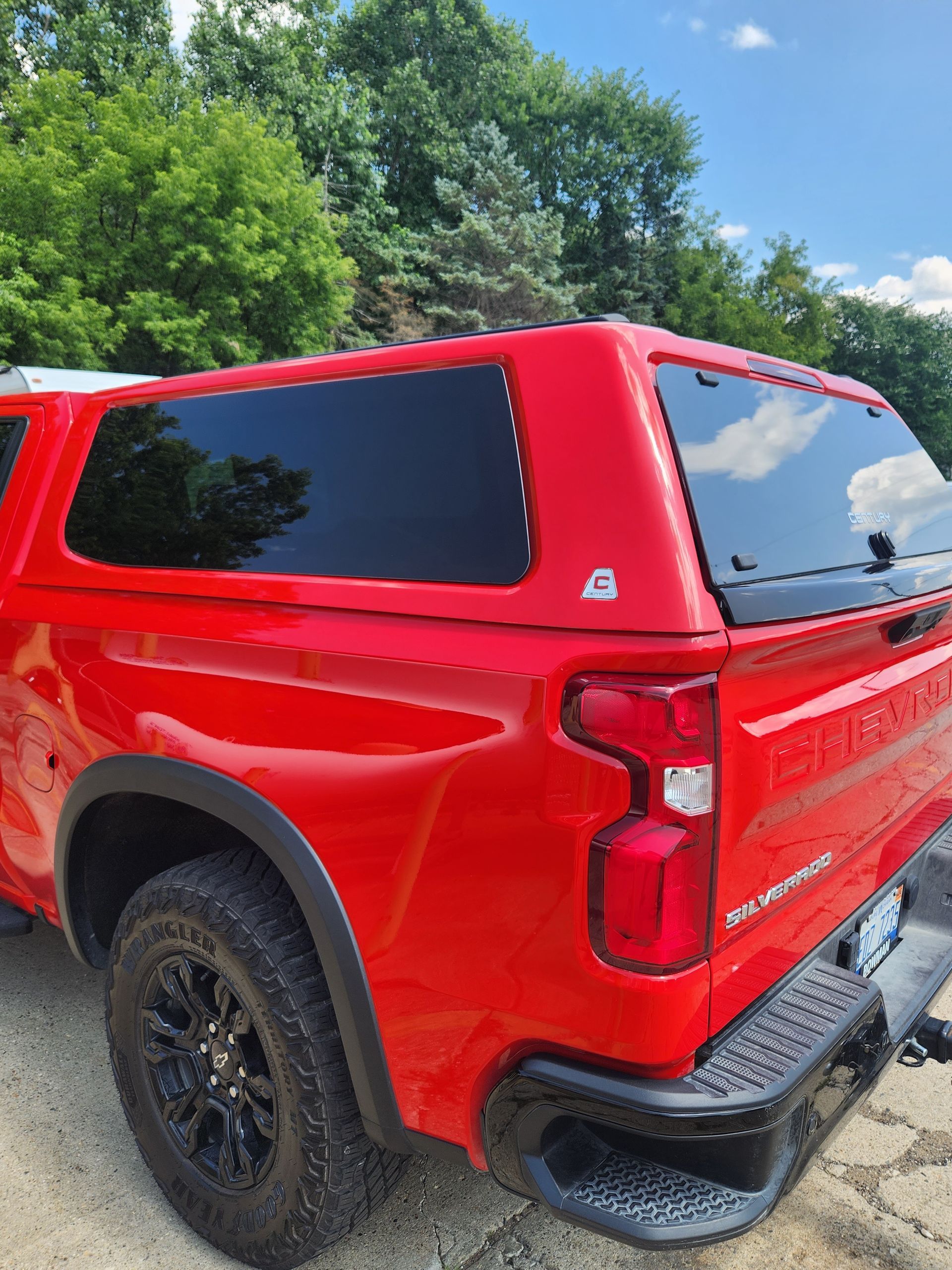 A red truck with a canopy on top of it is parked on a dirt road.
