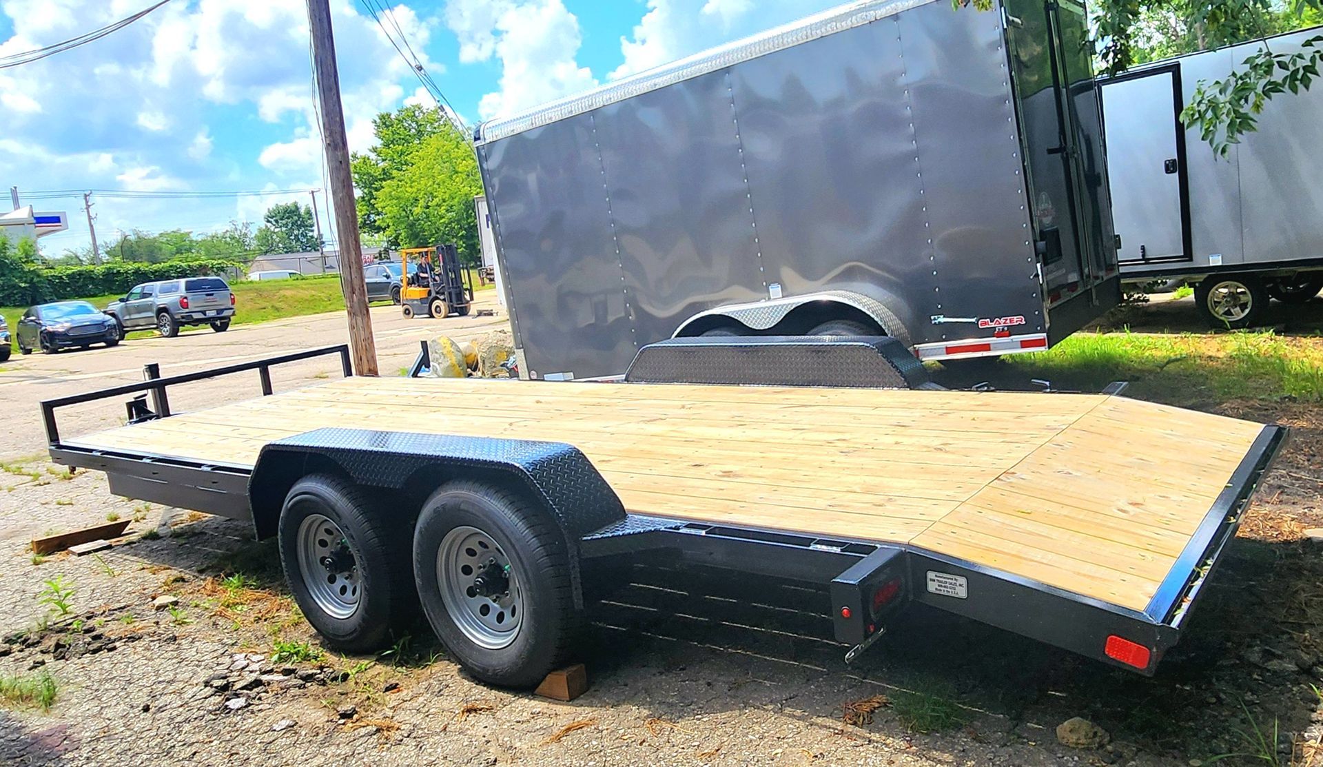A flatbed trailer is parked in a gravel lot next to a trailer.