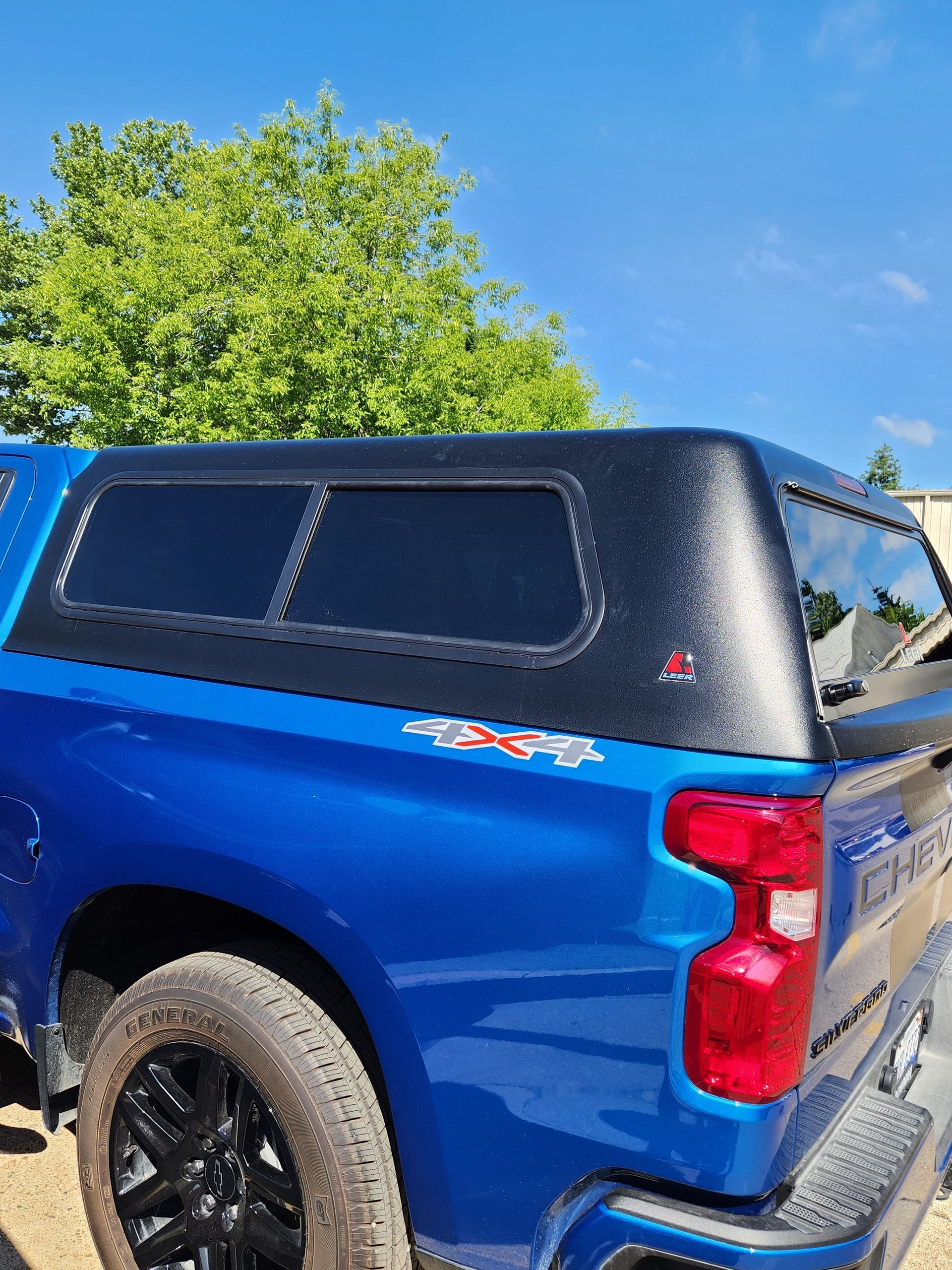 A blue truck with a black canopy is parked on the side of the road.