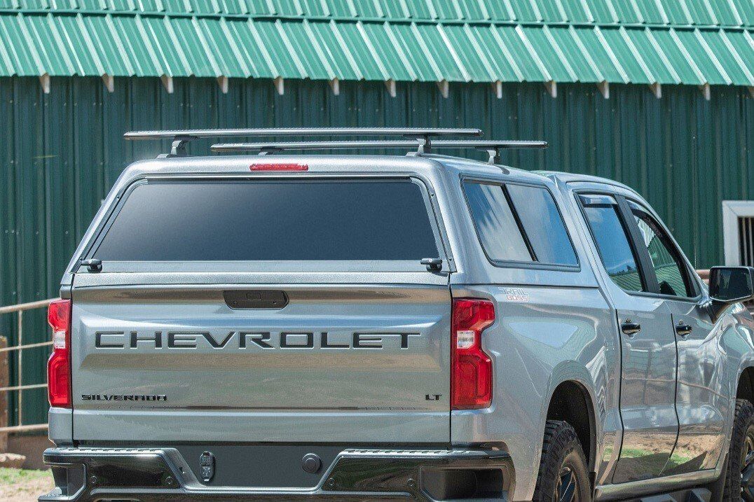 A silver chevrolet truck is parked in front of a green building.