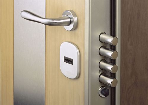 Stainless steel door with handle, keyhole, and multiple locking bolts; on a light wood background.