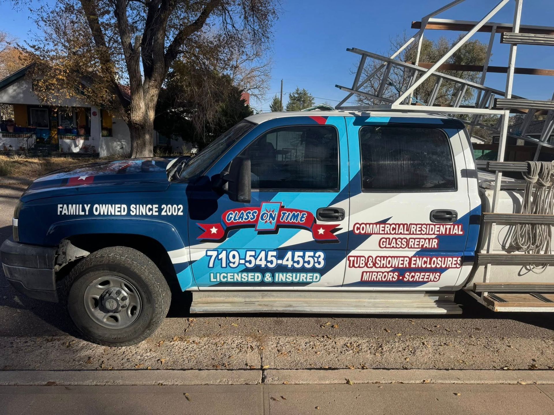 Blue and white work truck with logo and phone number; parked on a street.