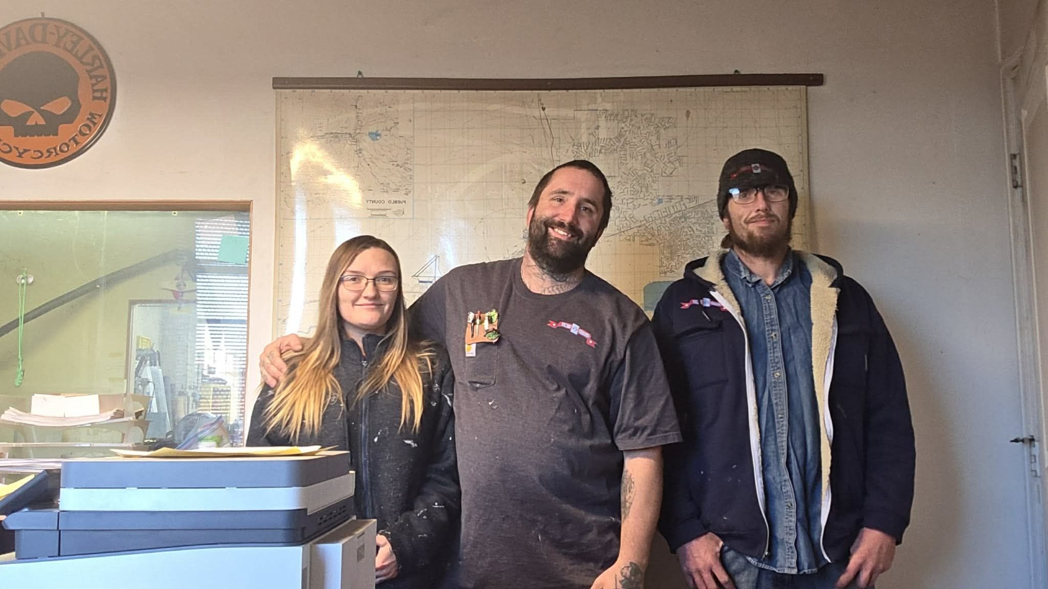 Three people posing in front of a printed map. One person has their arm around another.