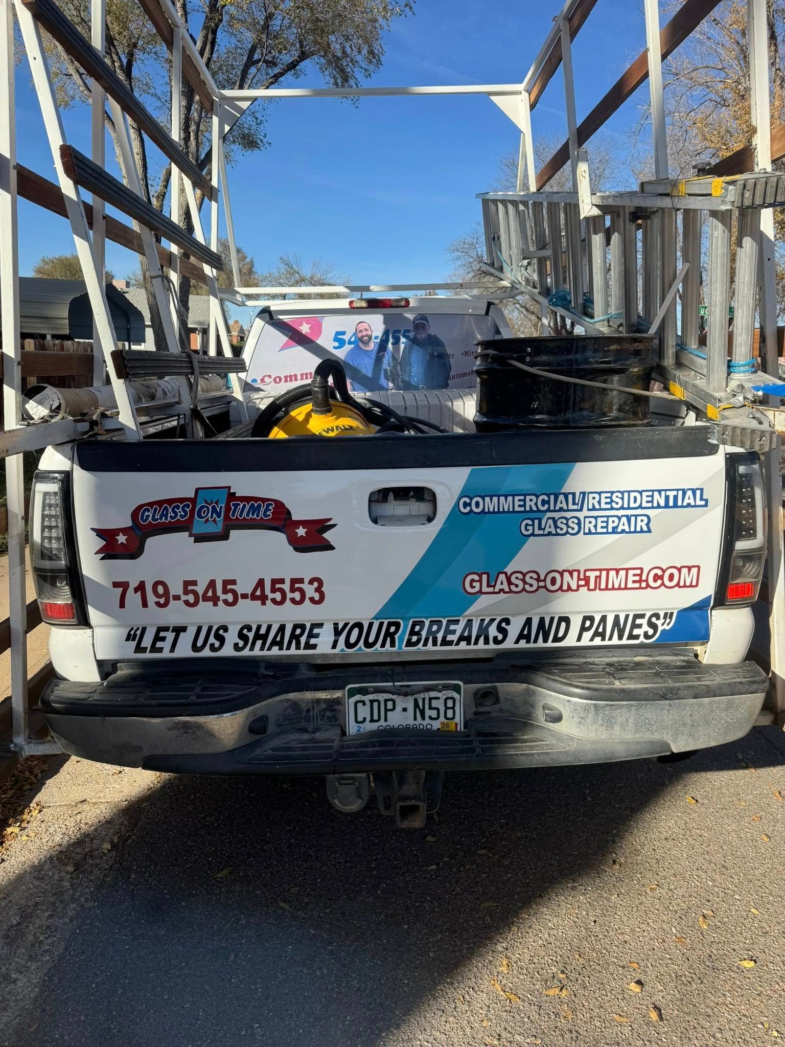 White pickup truck with business logo and phone number. Glass rack attached. Blue sky background.