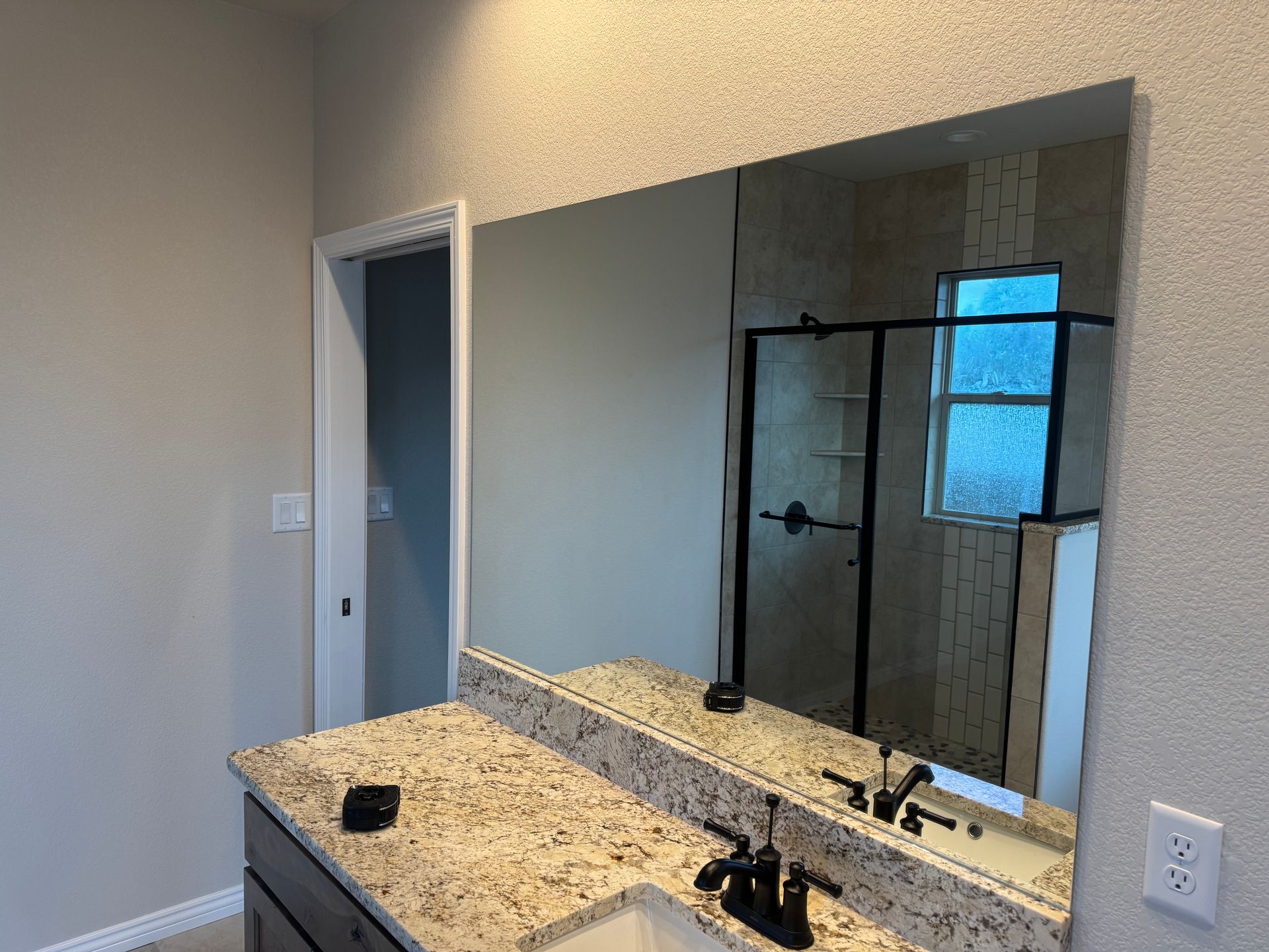 Bathroom with large mirror reflecting shower, granite countertop, and light-colored walls.