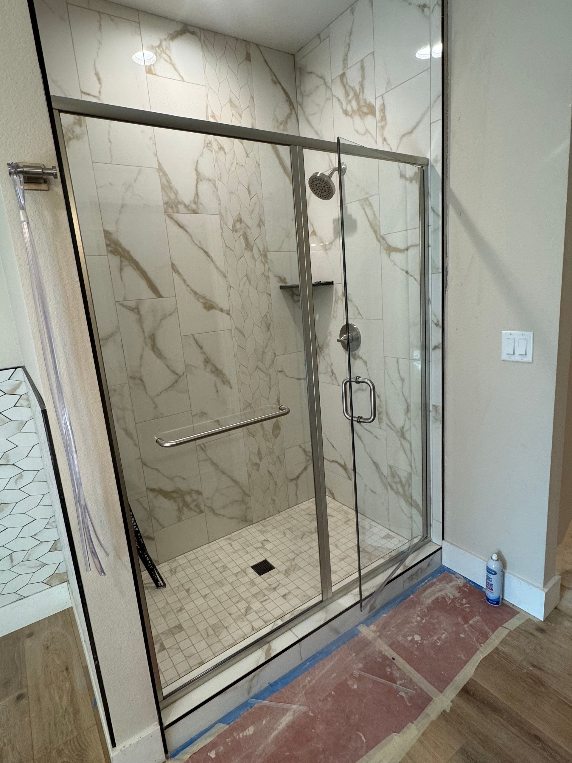Shower stall with marble-look tiles, glass doors, and chrome fixtures. 