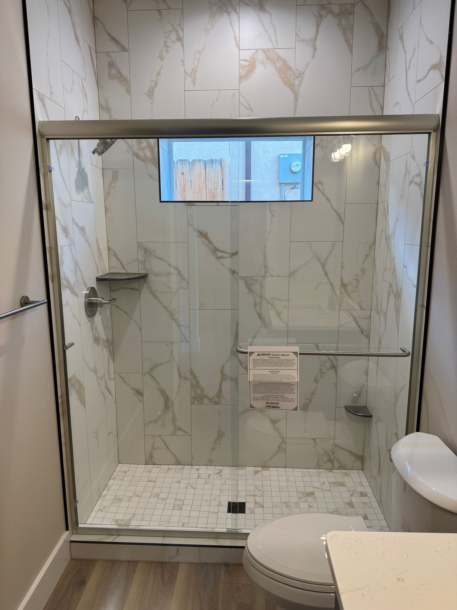 A modern shower with white marble-look tiles, glass door, and silver fixtures. 