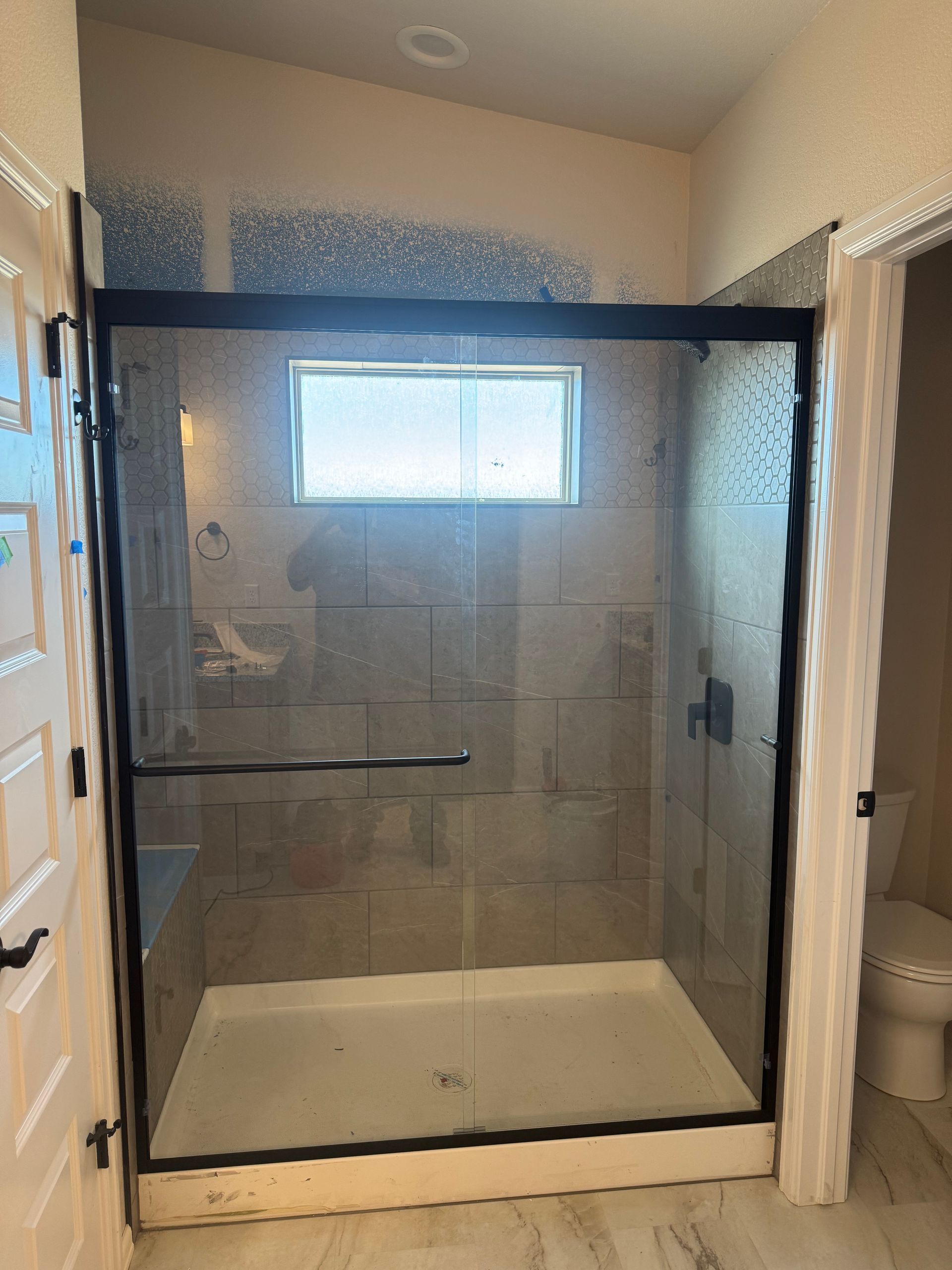 Shower with black frame, glass doors, tan tile, window, and white shower pan.
