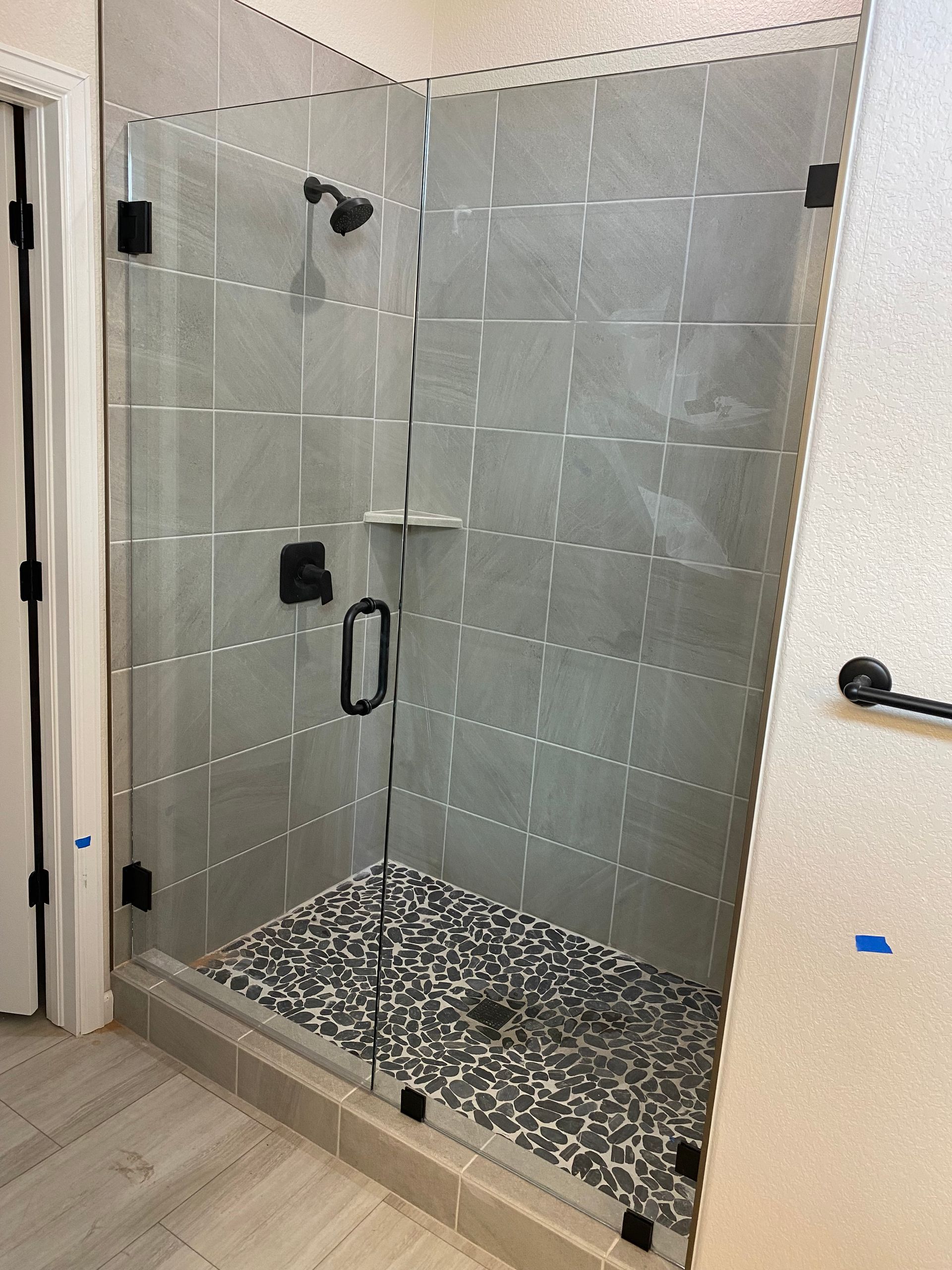 Glass shower enclosure with black fixtures and pebble floor.