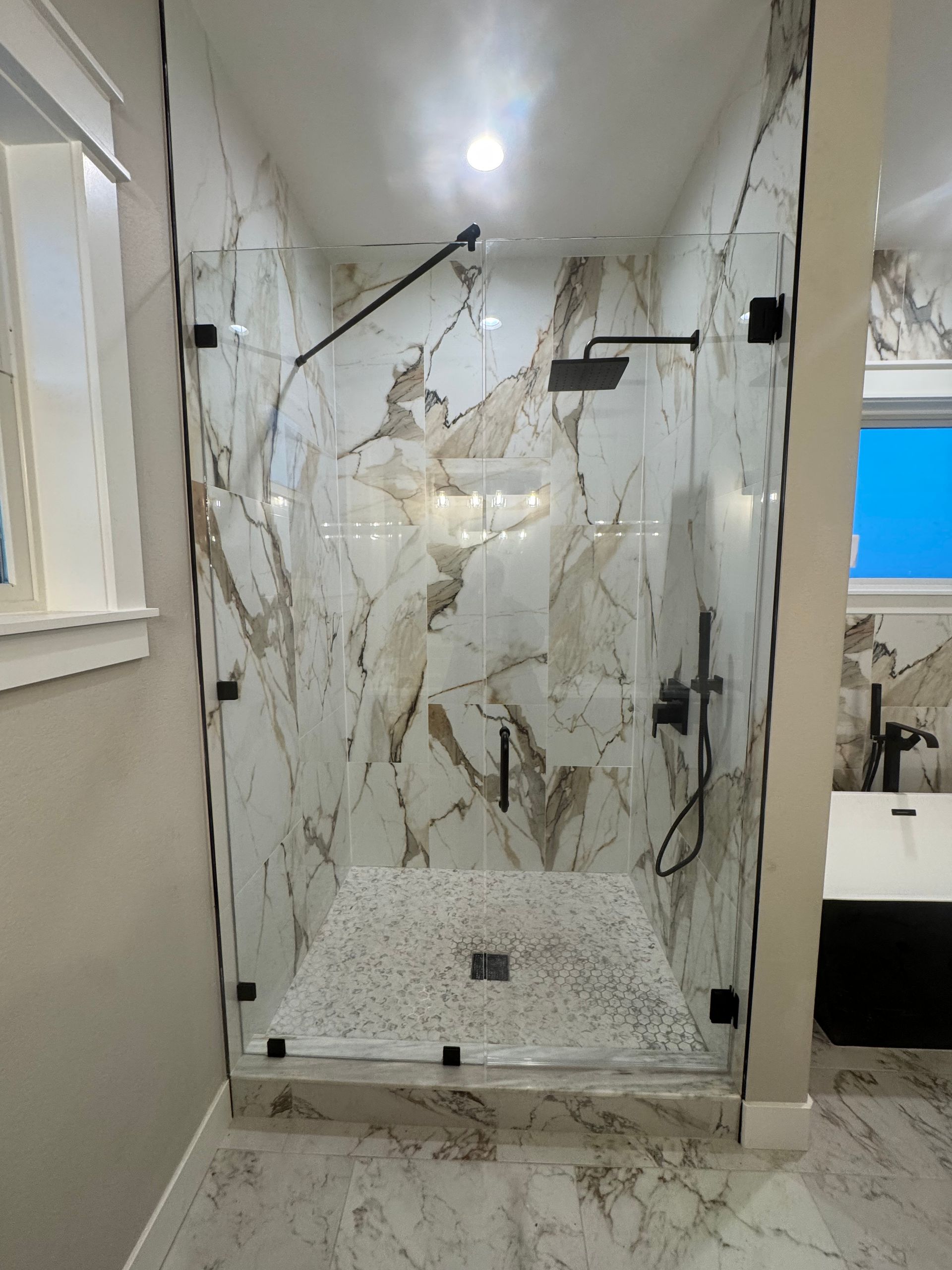 Shower enclosure with marble-patterned walls and floor, clear glass doors, black fixtures.