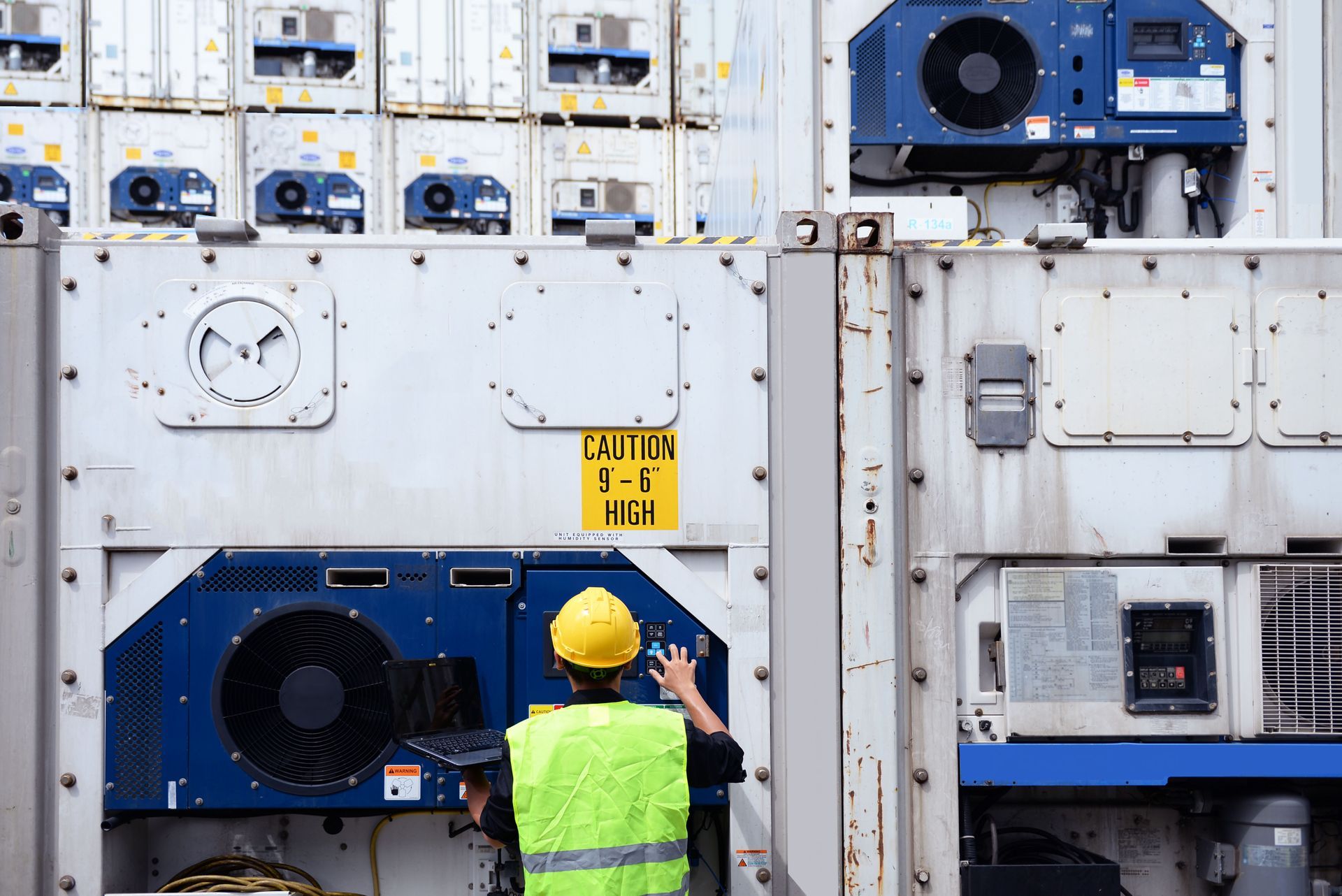 Worker in safety vest and hard hat checks refrigerated shipping containers.