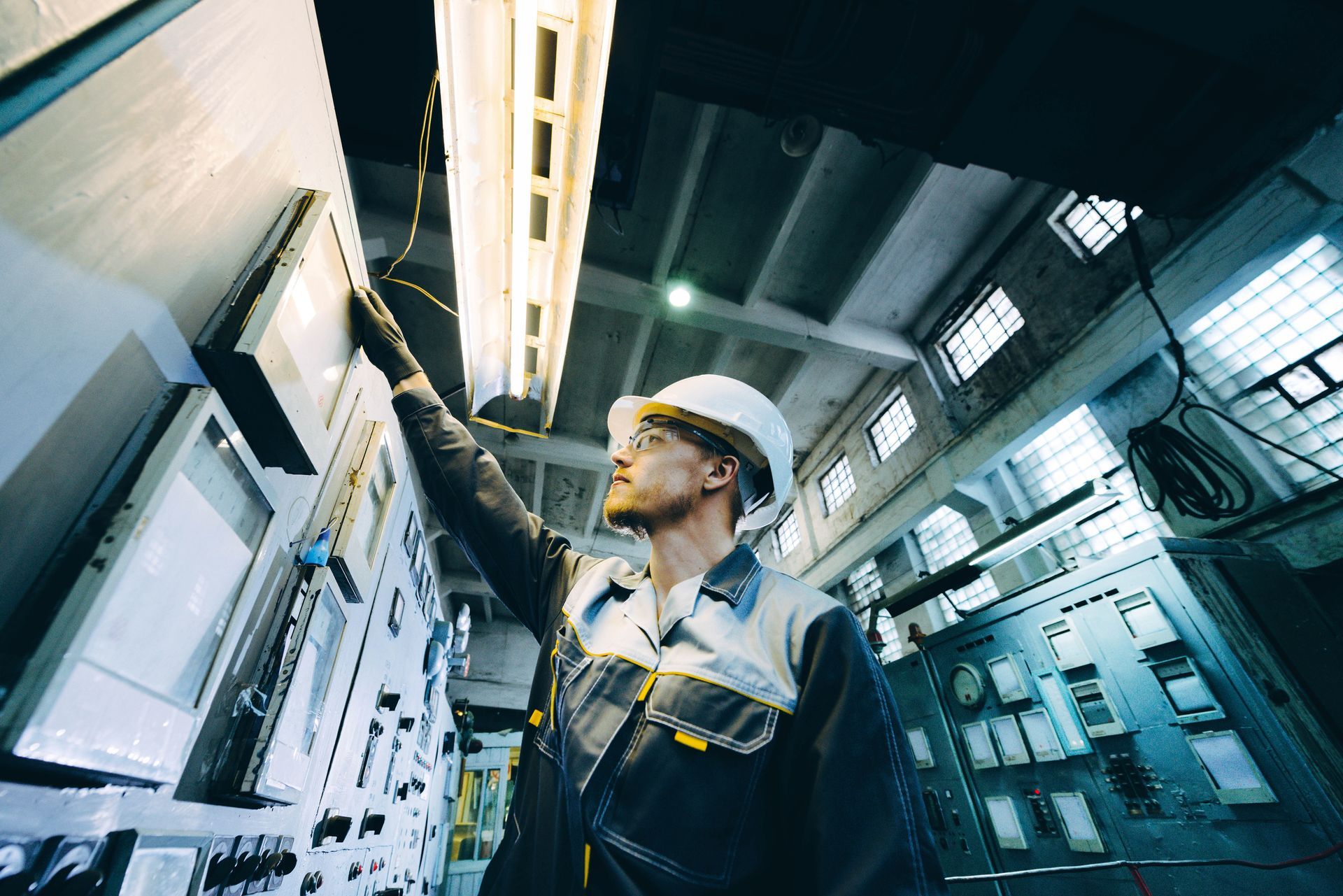 Man in hard hat working on control panel in industrial setting.