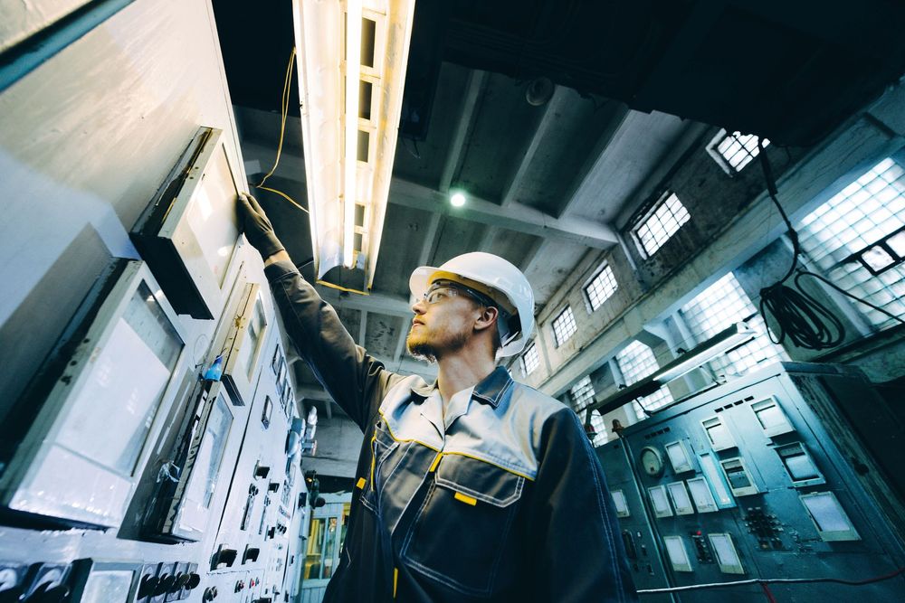Man in hard hat working on control panel in industrial setting.