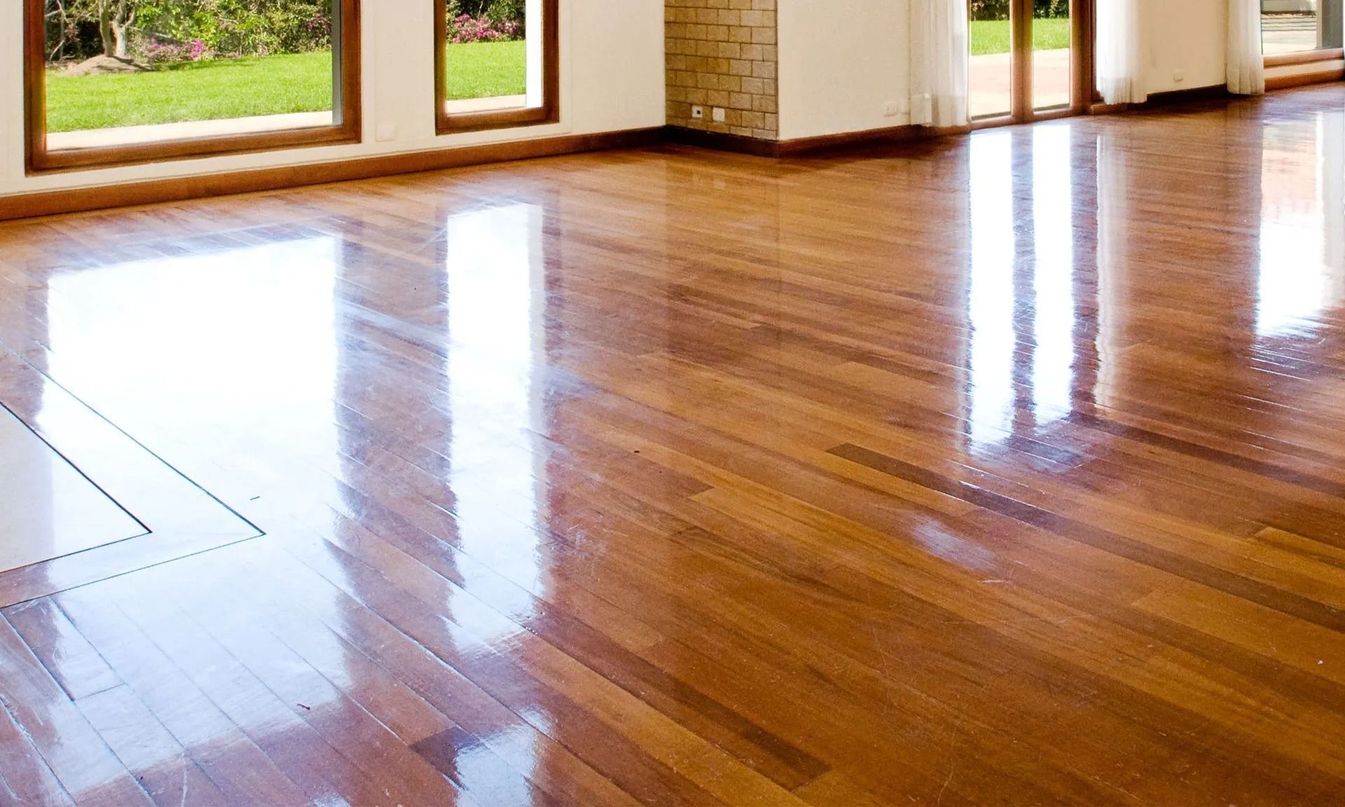 Highly polished wooden floor reflecting sunlight and windows in a bright interior.