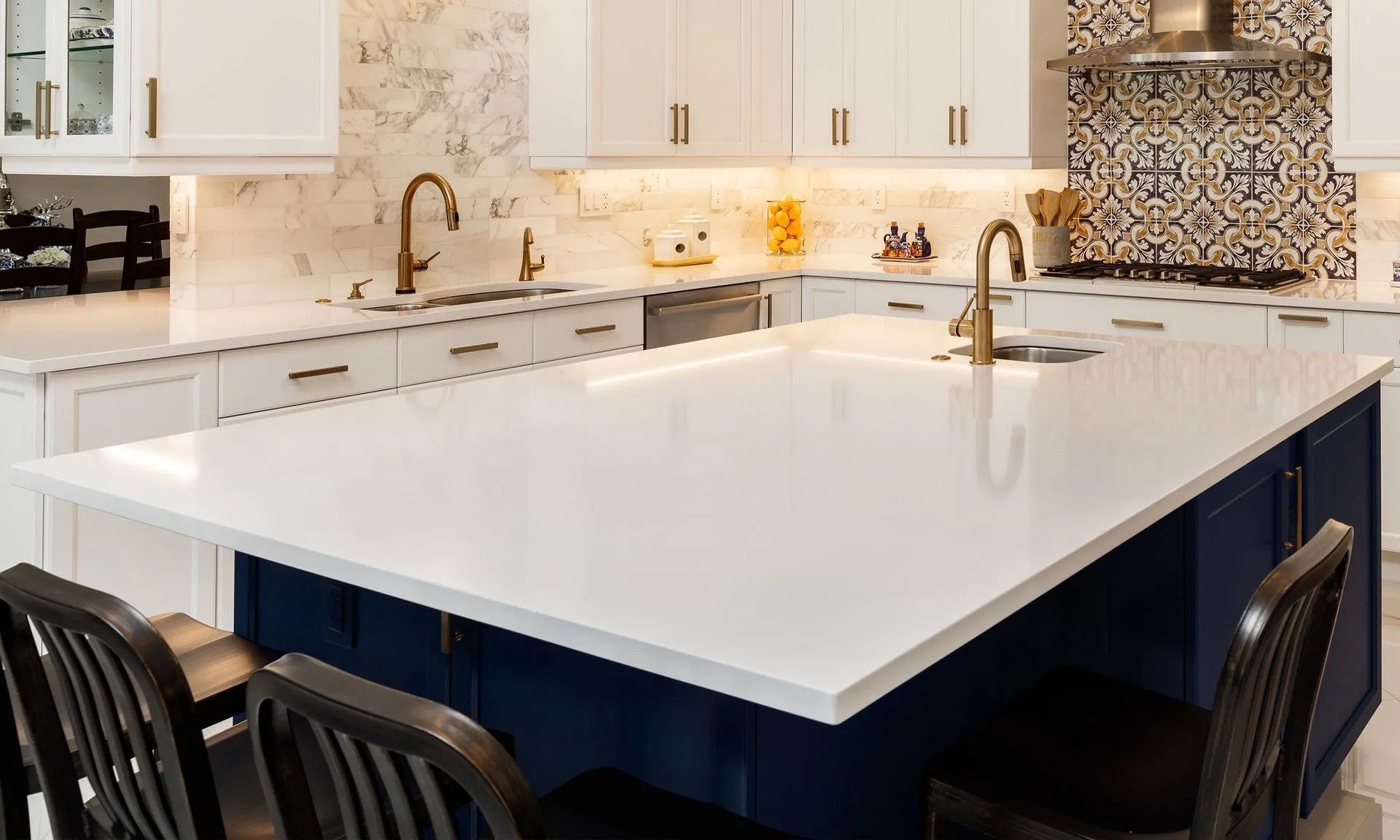 White countertop kitchen with blue island, gold fixtures, and patterned backsplash.