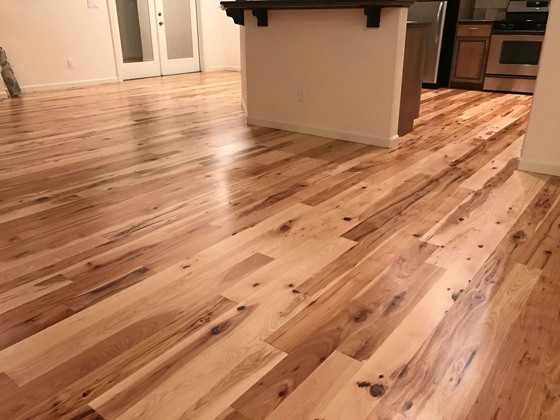 Light-colored hardwood floor in a room, angled view, with a kitchen island and doorway in the background.