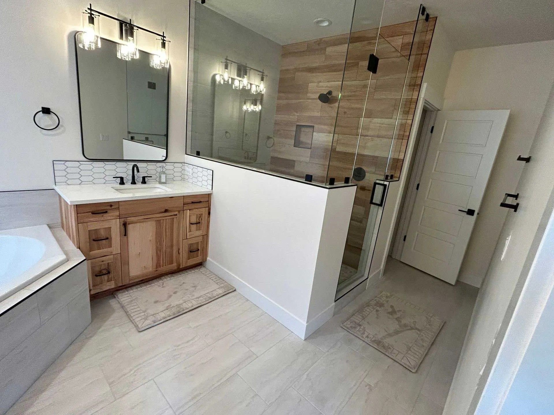 Modern bathroom with wood-look tile, glass shower, light wood vanity, and white walls.