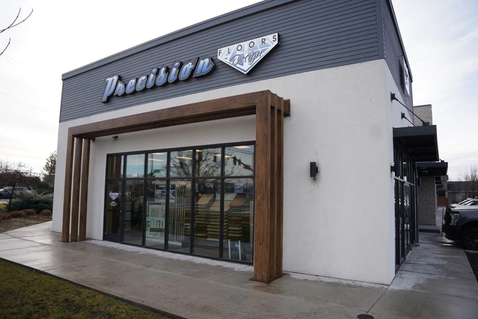 Exterior of Precision building; gray and white facade, brown wooden accents, glass storefront.