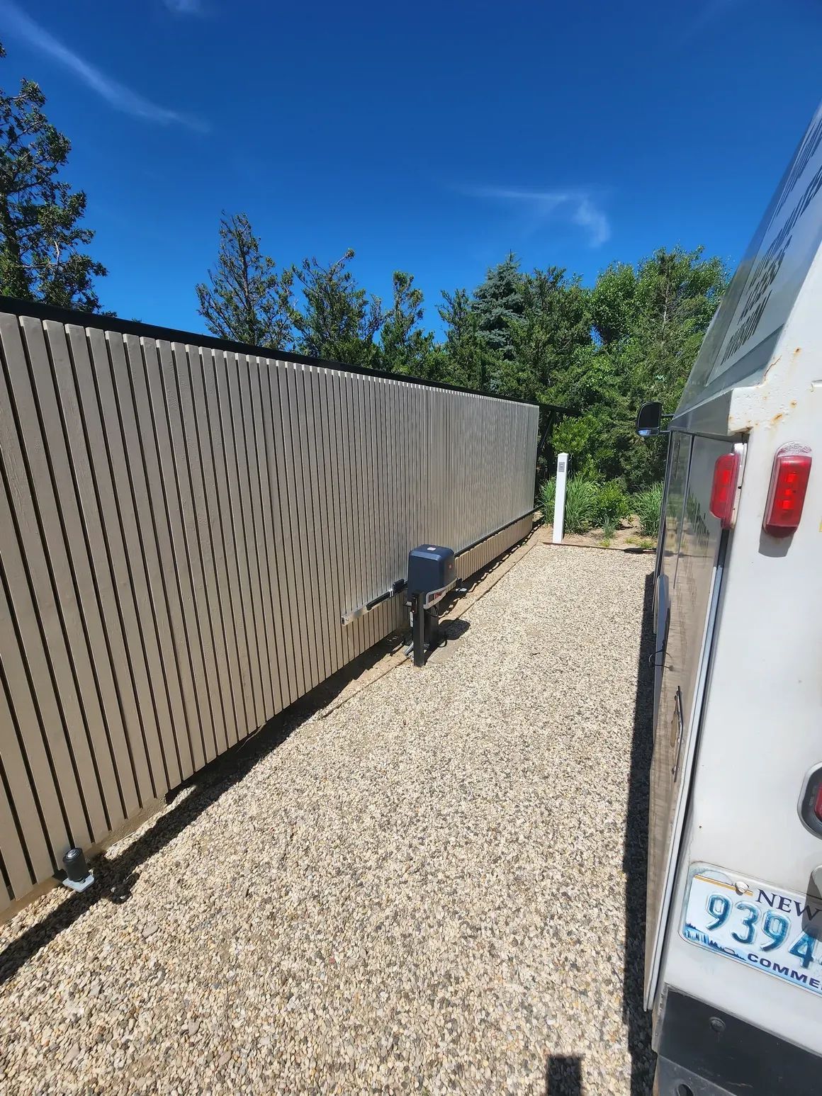 A white van is parked in a gravel driveway next to a fence