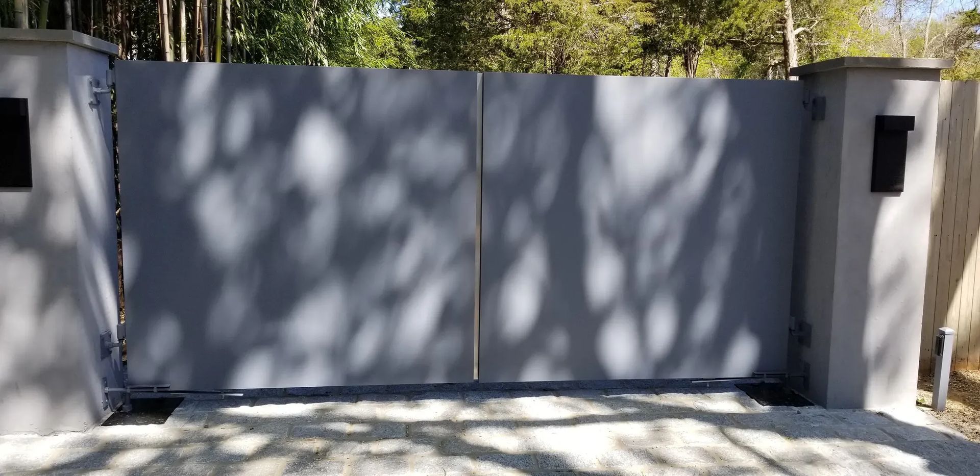 A gray gate with a mailbox on the side of it is surrounded by trees.
