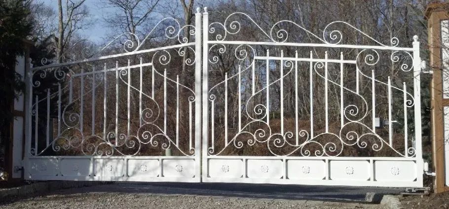 A white wrought iron gate is sitting on top of a gravel road