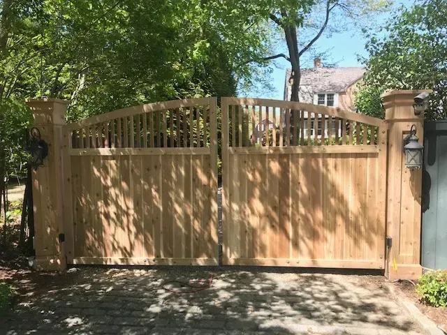 A wooden gate is sitting in the middle of a driveway next to a house.
