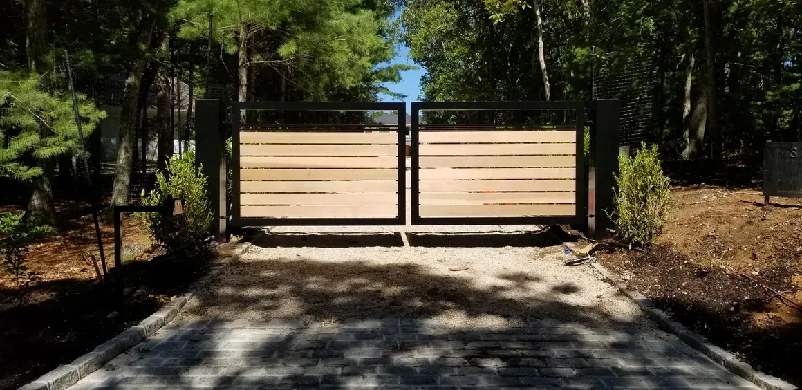 A wooden gate is sitting on the side of a dirt road in the middle of a forest.