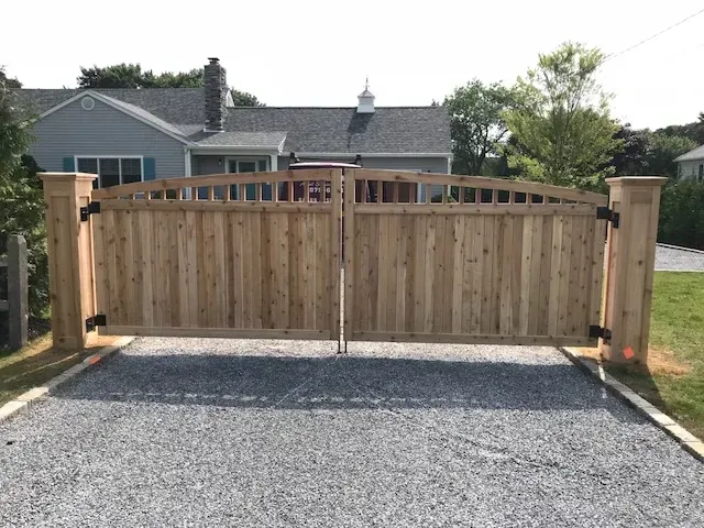 A wooden gate is sitting on top of a gravel driveway in front of a house.