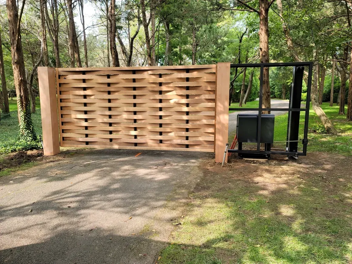 A wooden gate is sitting on the side of a road in the middle of a forest.