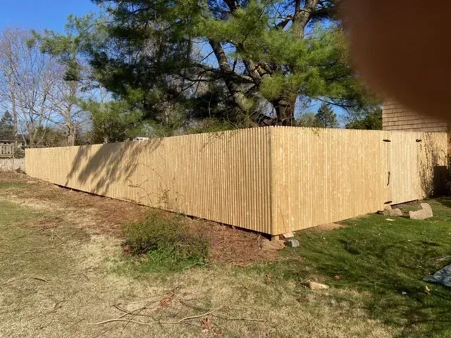 A wooden fence is sitting in the middle of a grassy field next to a house.