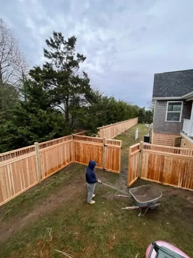 A man is standing in front of a wooden fence in a yard.