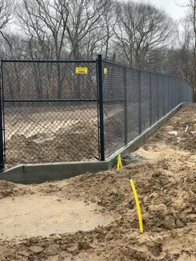 A chain link fence is being built in a dirt field.