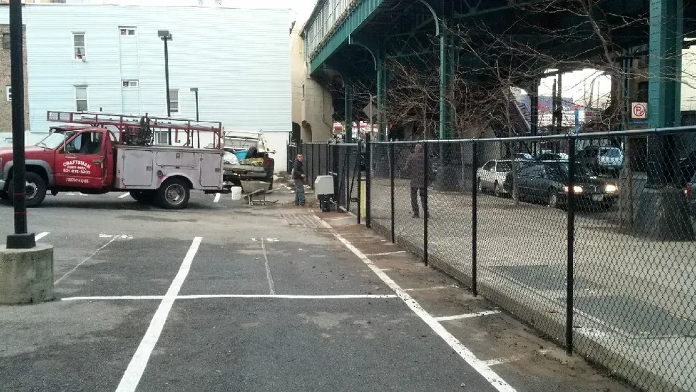 A red truck is parked in a parking lot next to a chain link fence