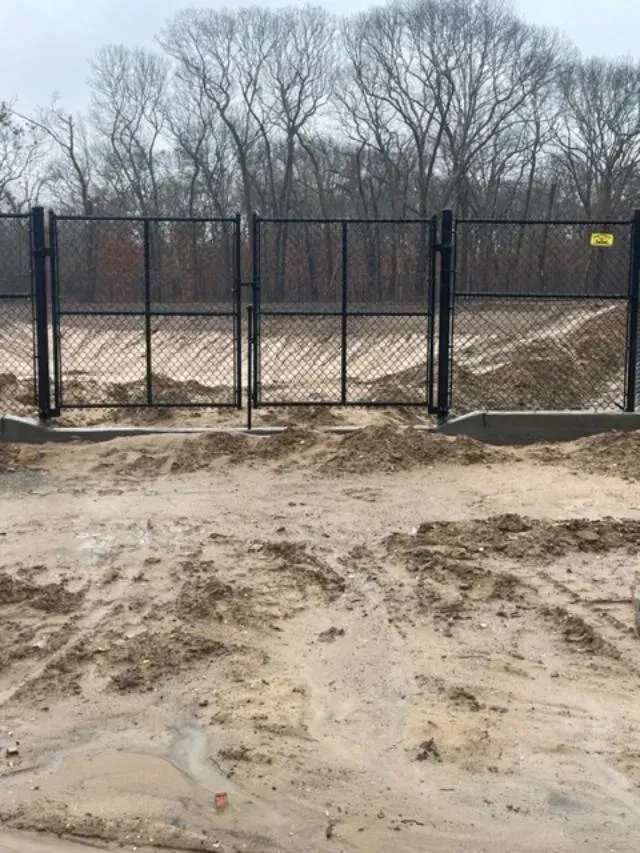 A metal fence is surrounding a dirt field with trees in the background.