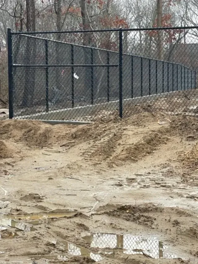 A chain link fence is being built in the middle of a muddy field.