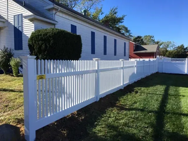 A white picket fence is in front of a white house.