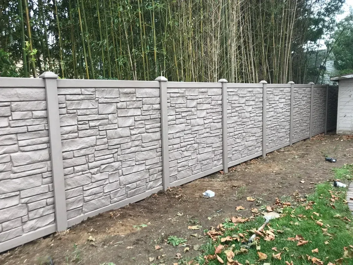 A stone fence is surrounded by trees in a backyard.
