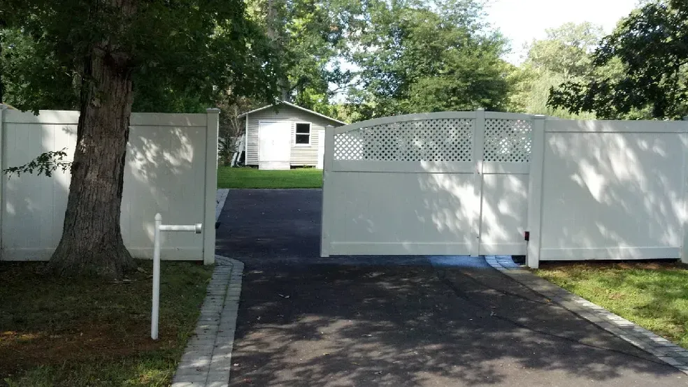 A white fence surrounds a driveway leading to a house.