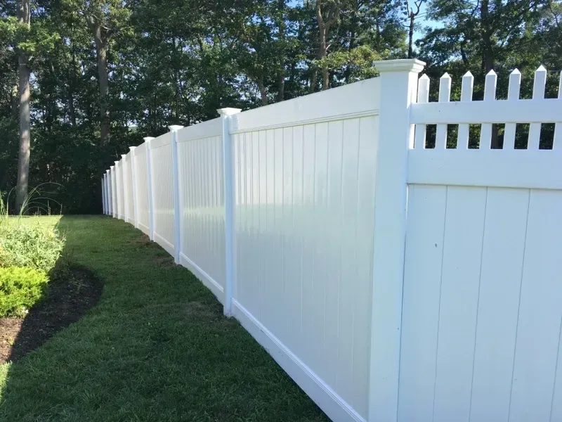 A white vinyl fence is sitting on top of a lush green lawn.