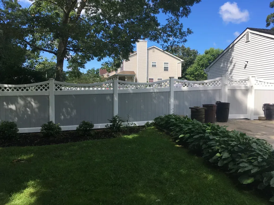 A white fence surrounds a lush green yard in front of a house.