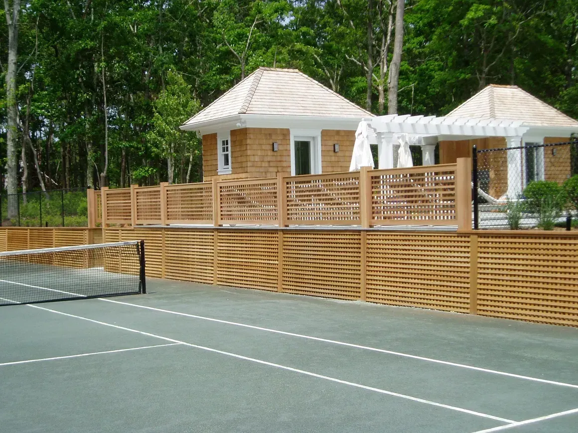 A tennis court in front of a house with a wooden fence