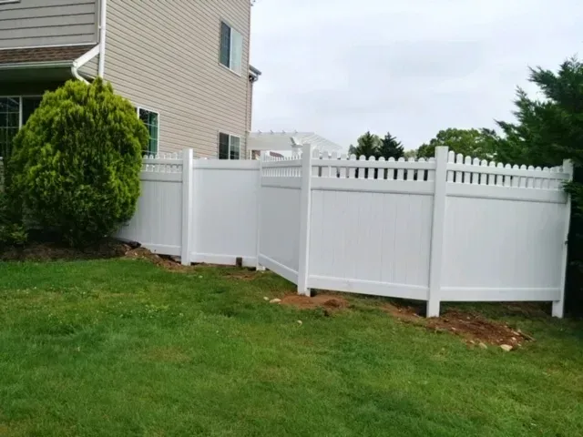 A white vinyl fence is in the backyard of a house.