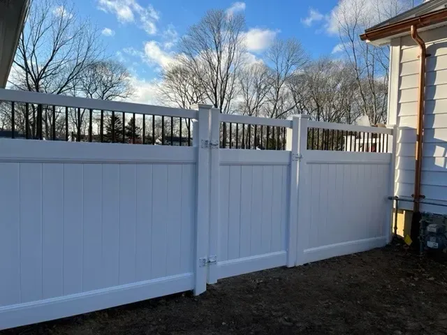 A white fence is surrounding a house with trees in the background.