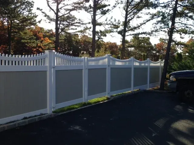 A white and grey fence with trees in the background