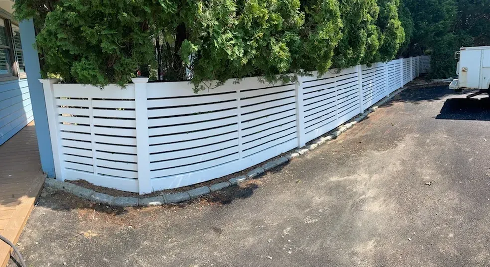 A white fence is surrounded by trees on the side of a road.